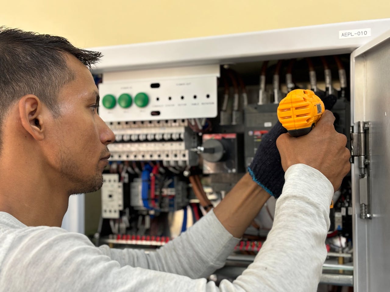 Skilled electrician using a drill to repair electrical equipment indoors. Focus on precision and safety.